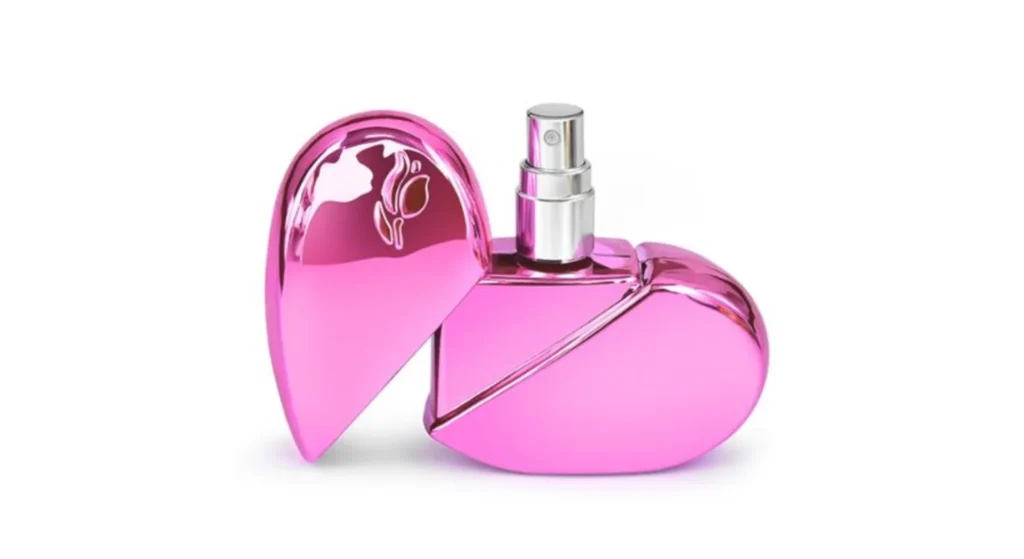A shiny, pink, heart-shaped glass perfume bottle with a silver spray nozzle is displayed with the cap off to the side, highlighting its unique perfume bottle shape against a white background.
