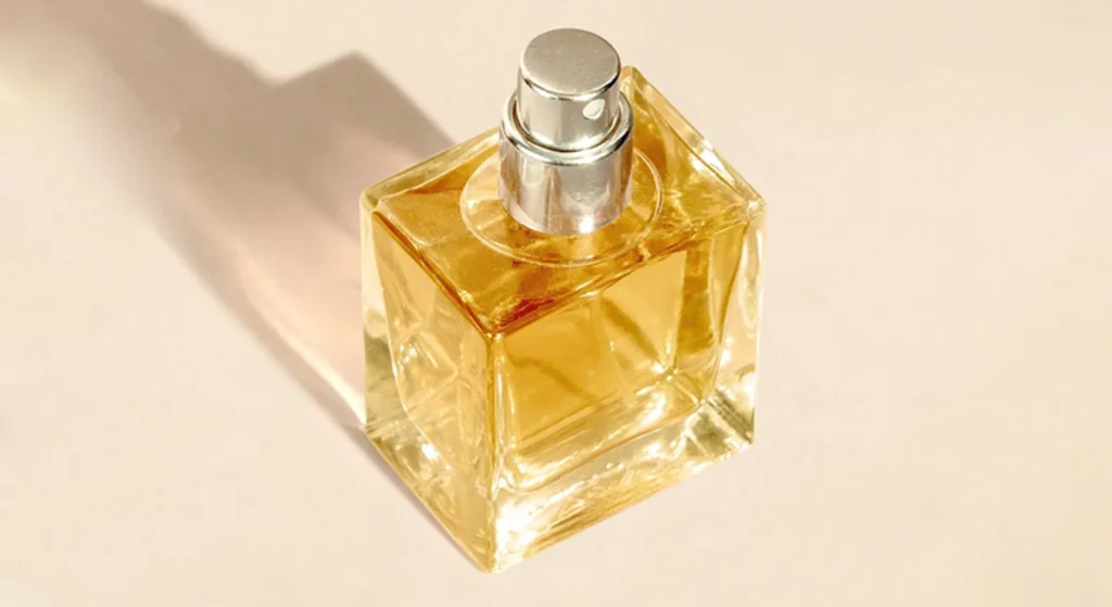 A square glass perfume bottle with a silver spray nozzle, filled with light amber liquid, casting a soft shadow on a neutral surface, showcasing one of the most popular square perfume bottle designs for elegant fragrances.