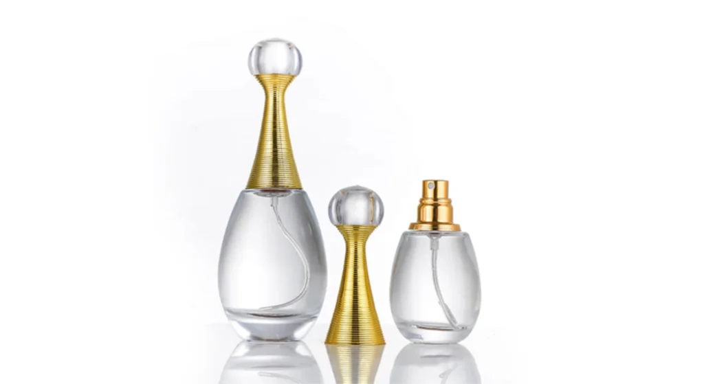 Three elegant tear drop shape perfume bottles with gold accents showcase stylish glass designs on a white background. One tall bottle has a round topper, while two shorter bottles feature a matching topper and an exposed spray nozzle.
